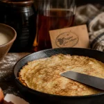 Origine des crepes : poêle en fonte et crêpe dorée sur plan de bois
